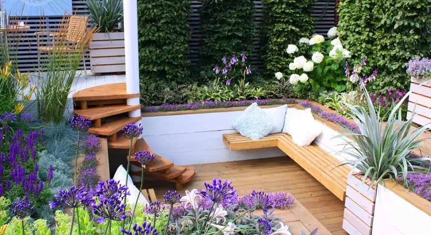 Magnifique terrasse en bois avec banquette intégrée, escalier en colimaçon et fleurs violettes. Idéal pour fabriquer banquette bois terrasse.