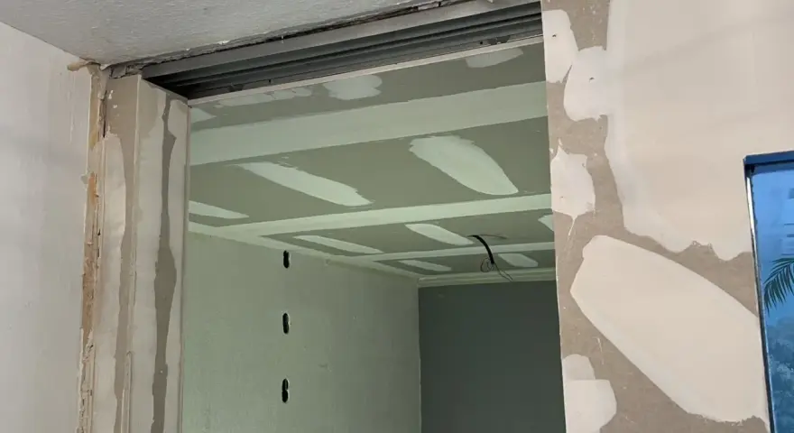 Ouverture dans un mur en cours de travaux de rénovation, avec plaques de plâtre et rails apparents.