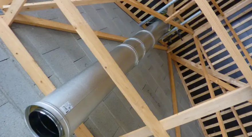 Installation d'un tubage cheminée en métal dans une charpente en bois. Le conduit traverse un mur en parpaings.