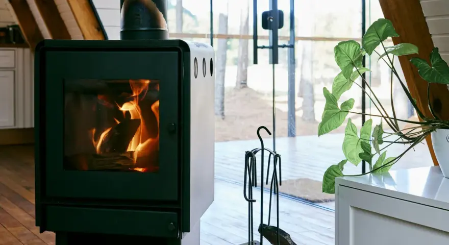 Un poêle à bois MCZ crépitant dans un chalet moderne, avec une grande baie vitrée donnant sur la forêt. Un avis positif s'impose pour ce coin cosy.