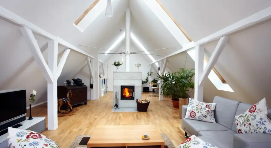 Aménagement comble 30m2 : salon cosy avec cheminée, canapé gris, parquet clair et poutres apparentes.