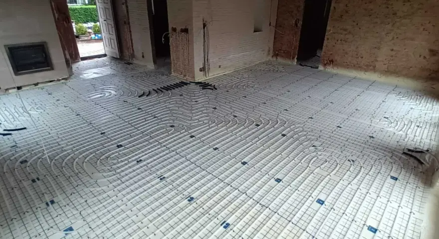 Installation d'un plancher chauffant en cours de renovation. Les tuyaux blancs sont posés sur des panneaux isolants, prêts à être recouverts.
