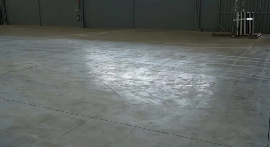 Vaste entrepôt avec une dalle béton qui part en poussière, marquée par des traces de passage.
