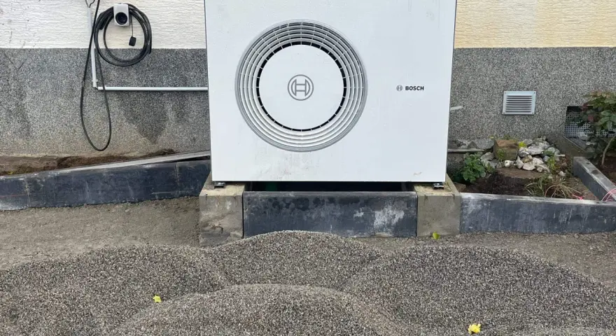Unité extérieure d'une chaudière à condensation Bosch, installée sur des blocs de béton, avec un chargeur mural à proximité.
