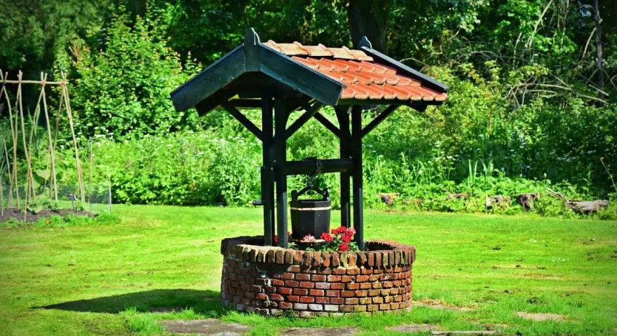 Un puits de briques rouges, orné de fleurs, avec un seau suspendu, prêt à creuser un puits pour abreuver le jardin verdoyant.