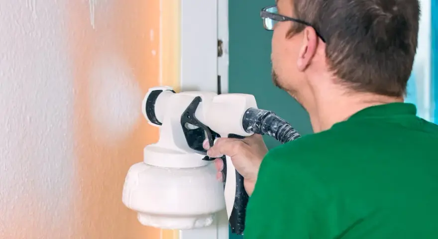 Un homme en t-shirt vert utilise un pistolet pour peindre un mur en orange.