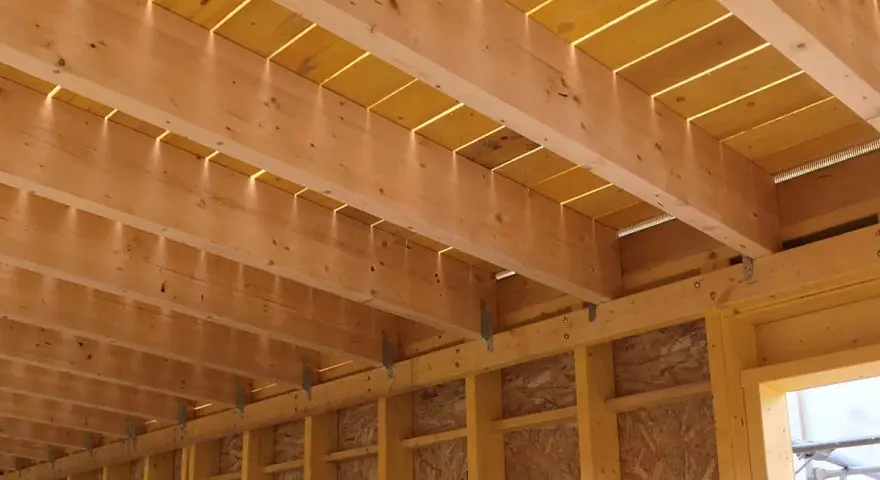 Vue détaillée de comment réaliser le solivage d'un plancher d'étage : poutres en bois, panneaux jaunes et supports métalliques.