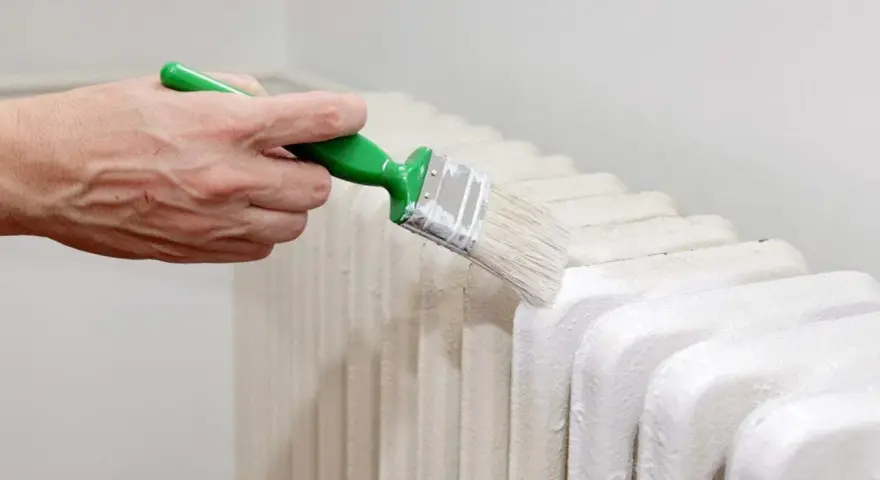 Main d'une personne peignant un radiateur en fonte avec une brosse.