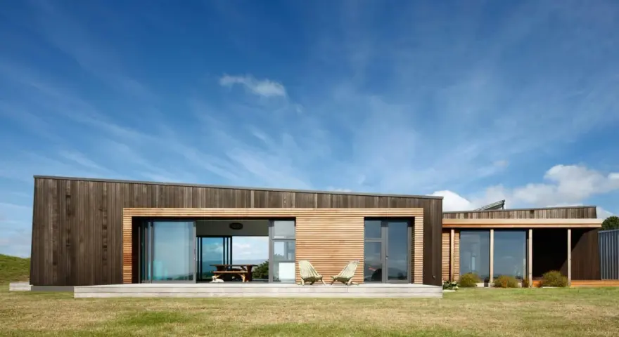 Maison moderne en bois avec grande baie vitrée, deux chaises invitantes sur la terrasse. Une extension maison container stylée.