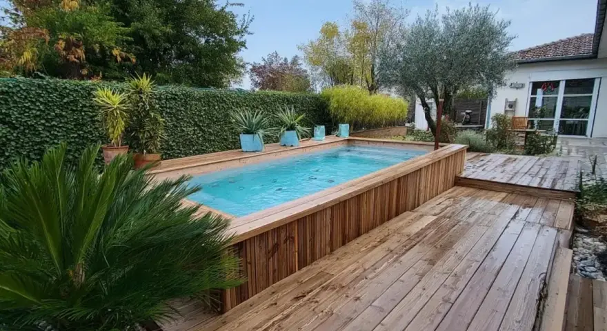 Aménagement abord piscine hors sol en bois, avec terrasse et végétation luxuriante.