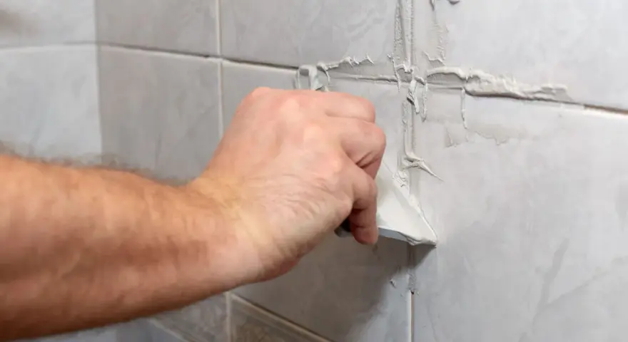 Main tenant enlève du joint de carrelage sec avec une spatule.