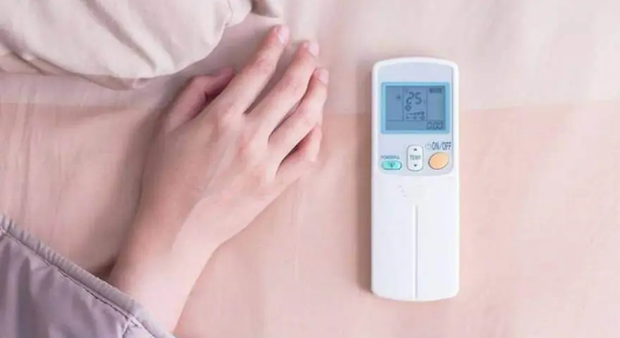 Main tenant ajuste la température clim pour dormir. La télécommande affiche 25 degrés.