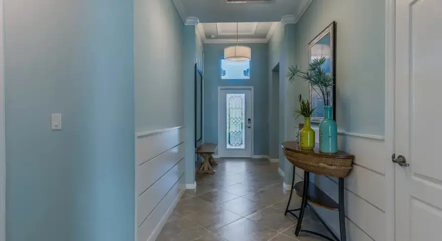 Un couloir lumineux avec une peinture de couloir 2 couleurs : bleu ciel et blanc. Un banc, une console avec des vases et une porte vitrée ornent cet espace accueillant.