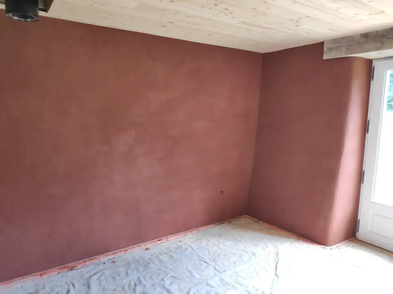 Un coin de pièce aux murs recouverts d'un bel enduit chaux sable ocre. Le sol est protégé par une bâche.
