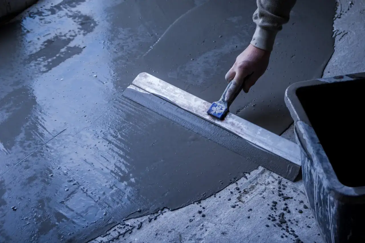 Main tenant utilise une taloche pour le ragr&eacute;age d'une terrasse ext&eacute;rieure avec pente.