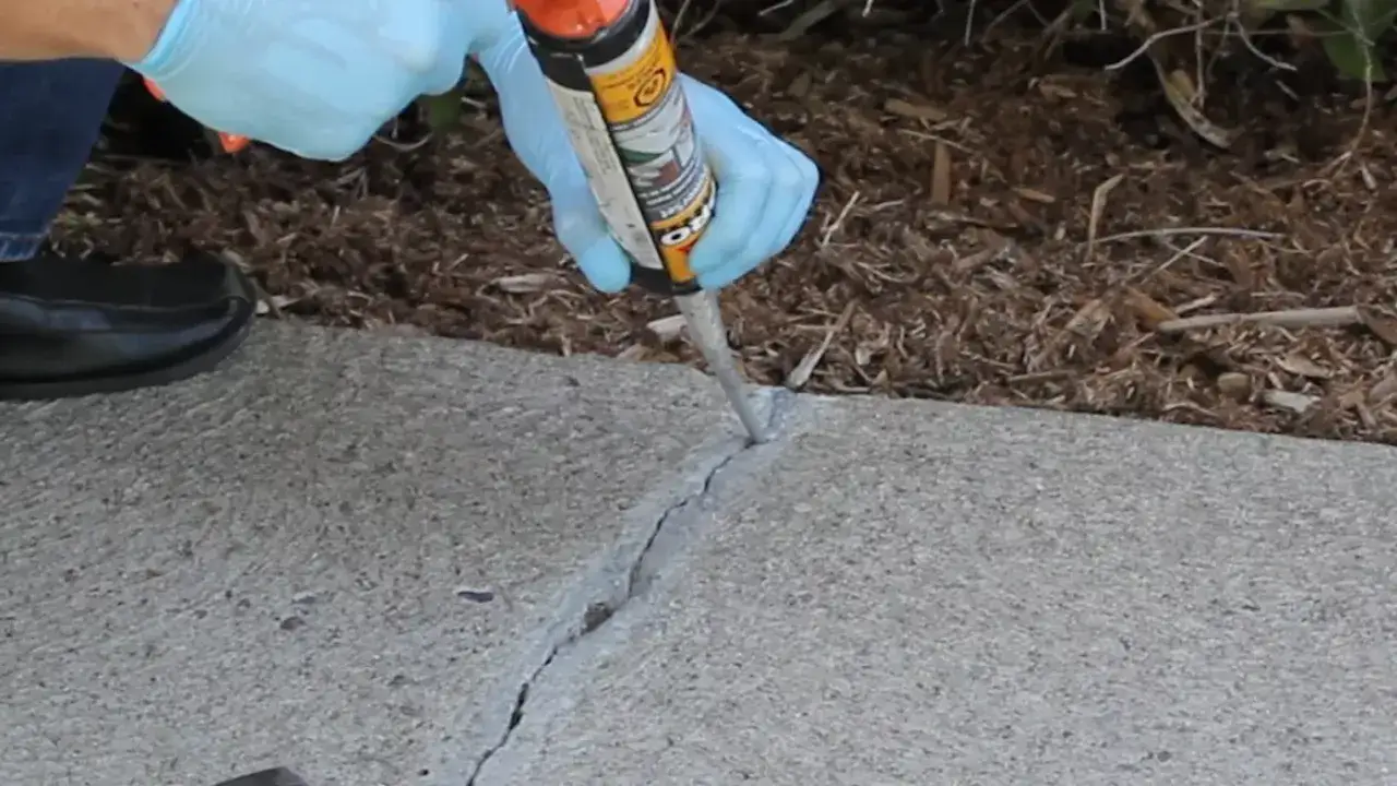Application d'un produit de réparation dans une fissure de dalle en béton.