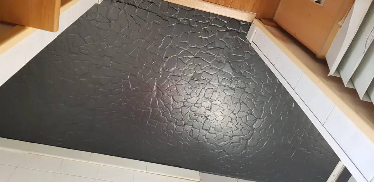 Un carrelage usé que faire ? Ce revêtement texturé gris foncé, imitant des pierres irrégulières, est posé au sol.