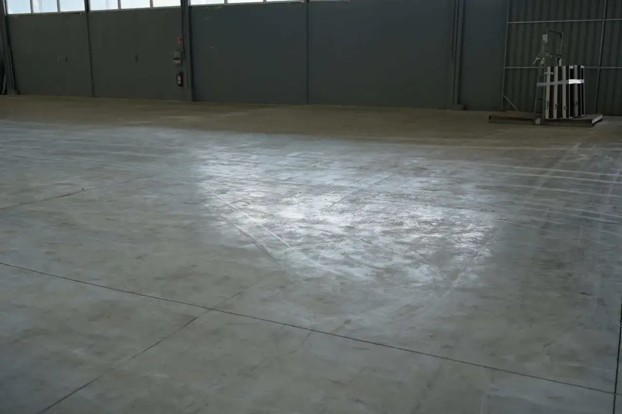 Un grand entrepôt avec une dalle béton qui part en poussière, marquée par des traces de passage.