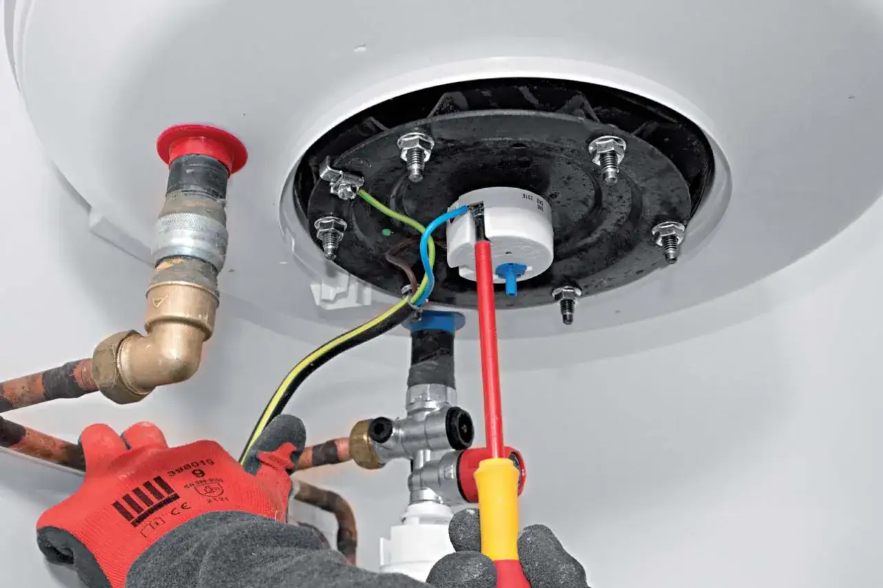 Main tenant installe un ballon d'eau chaude, connectant les fils électriques et les tuyaux de cuivre.