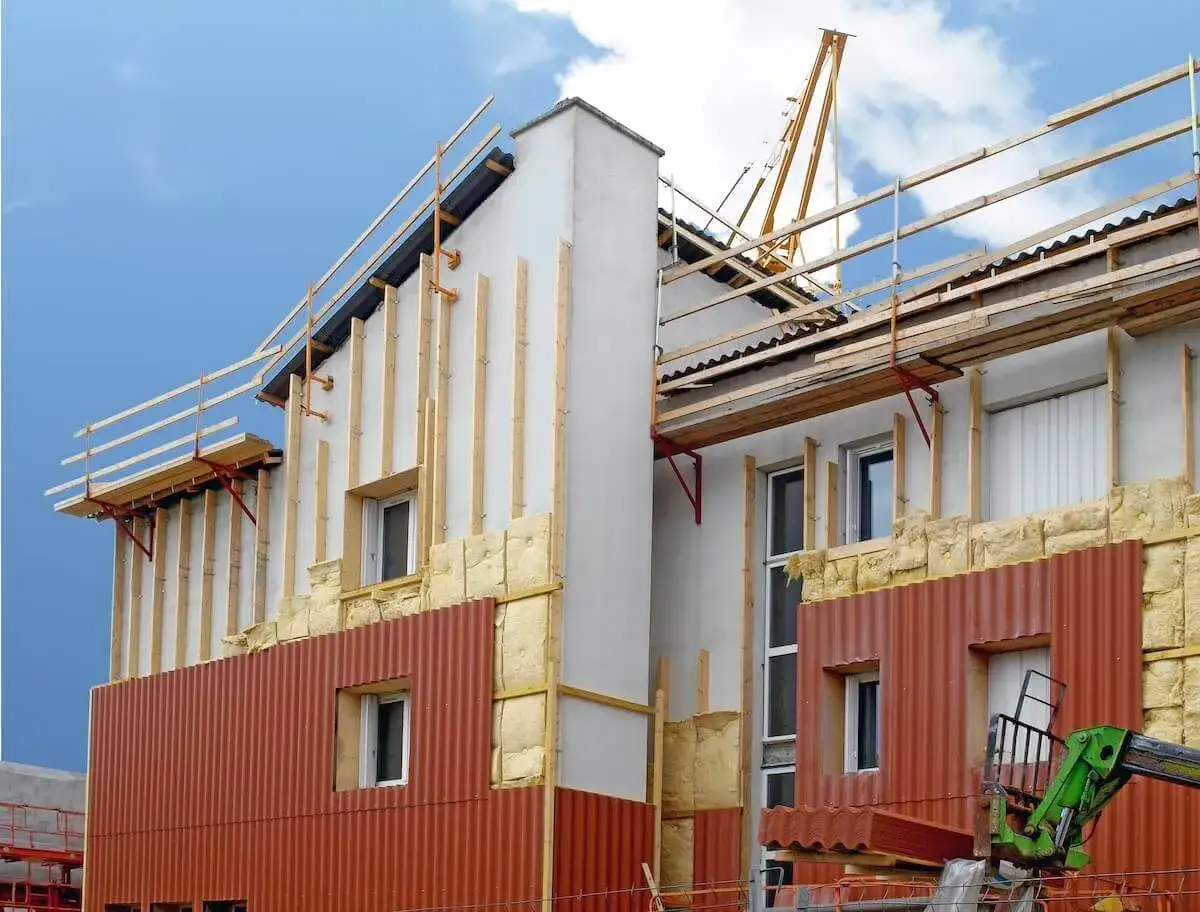 Chantier de ravalement avec isolation extérieure en cours. Des panneaux de bardage rouge et de la laine de roche sont visibles.