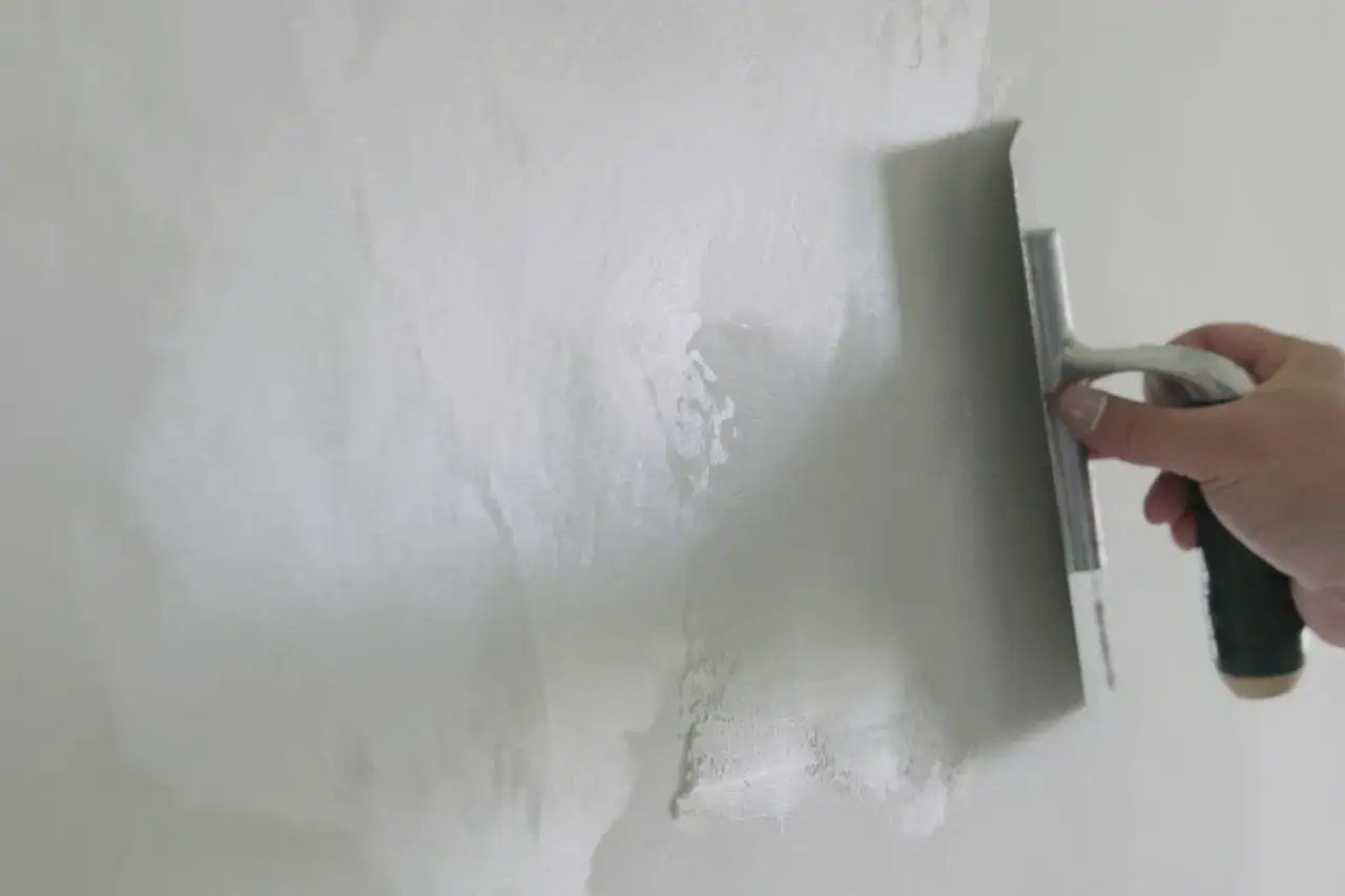 Main tenant une taloche, il applique un enduit sur un mur. Une démonstration de comment faire un enduit sur un mur.
