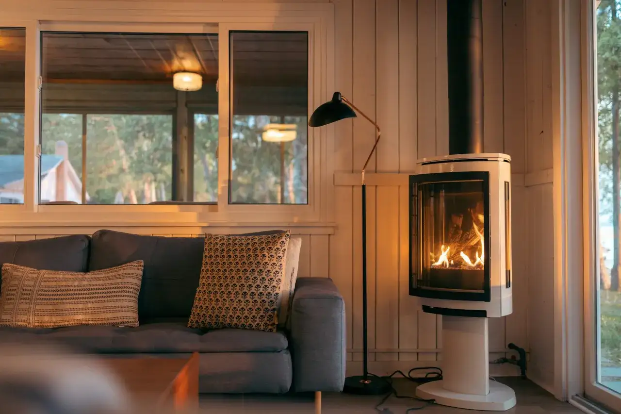 Un poêle à bois moderne, avec un feu vif, est placé à distance du mur en placo. Un canapé confortable invite à la détente près de la chaleur.