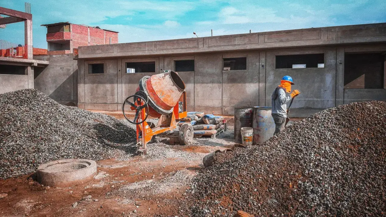 Chantier de construction avec bétonnière, sacs de ciment et ouvrier. Le dosage béton est essentiel pour la solidité.