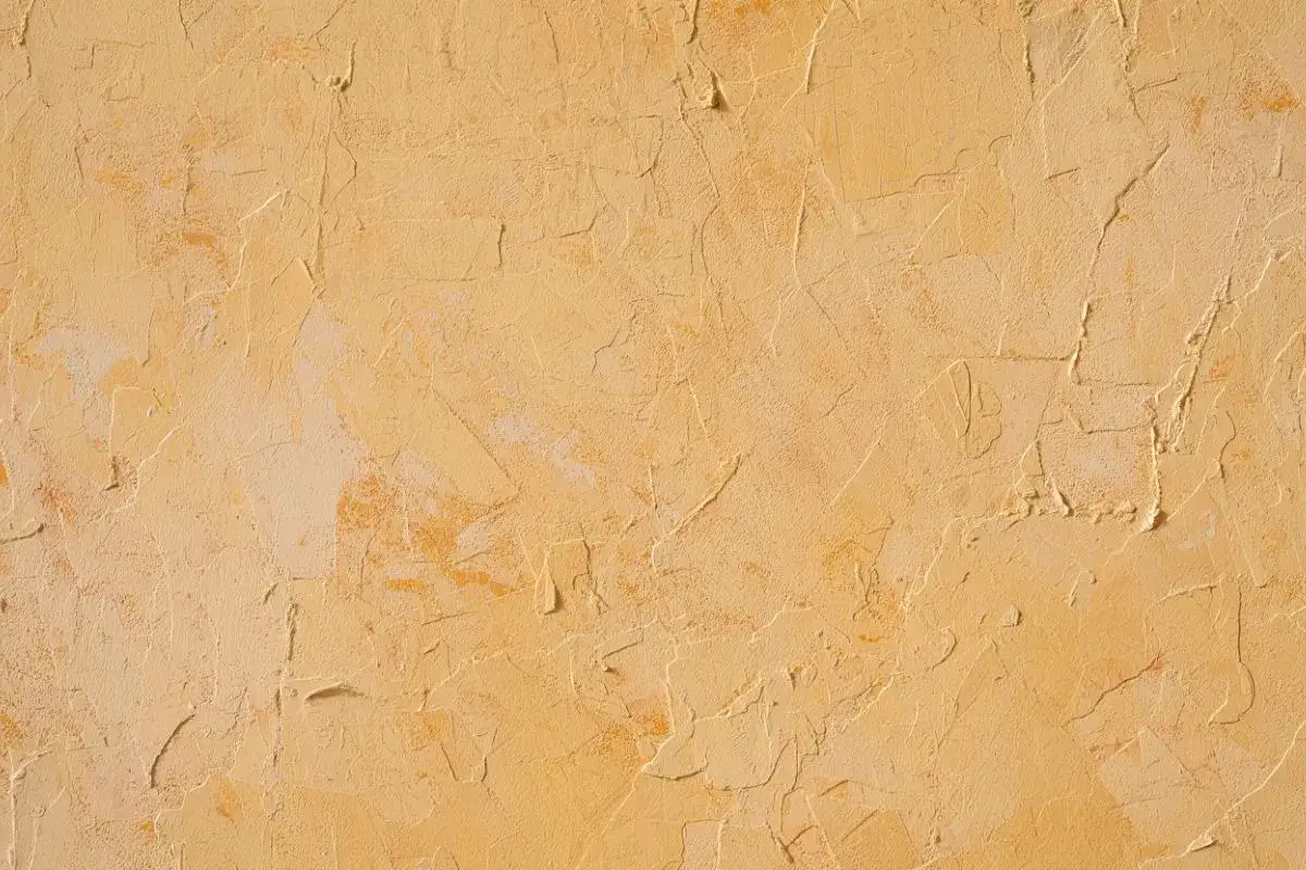 Texture d'un mur avec un enduit taloché ou gratté, aux nuances chaudes de jaune et d'ocre, évoquant un style rustique et chaleureux.