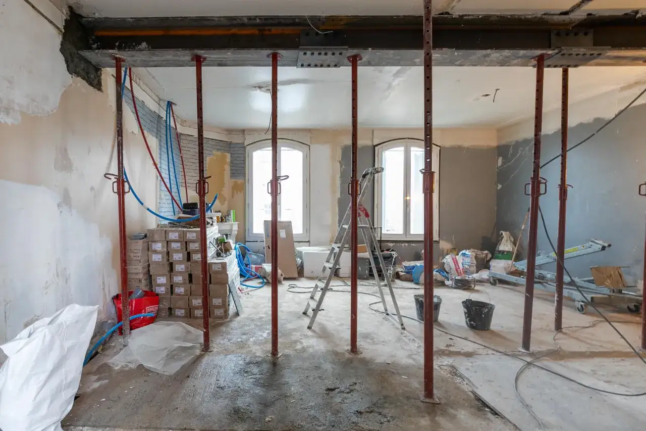 Chantier en cours pour rénover sa maison. Des étais soutiennent le plafond, des matériaux sont empilés, une échelle est présente.
