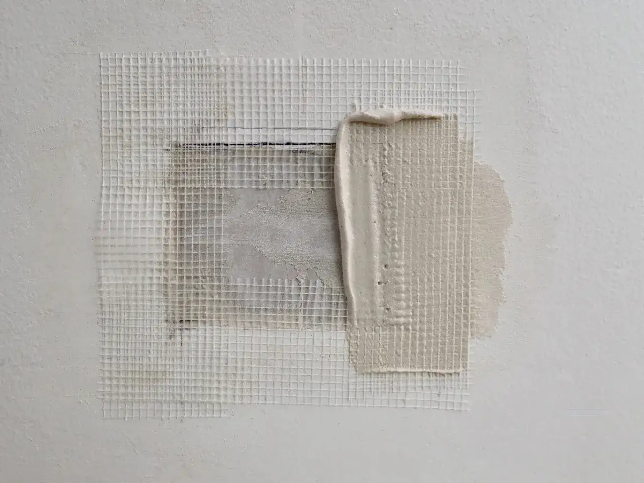 Application de mortier sur une grille pour reboucher un trou dans un mur.
