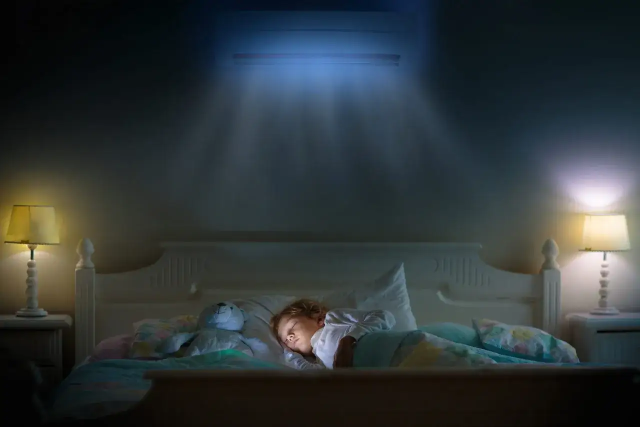 Un enfant dort paisiblement sous un climatiseur diffusant une douce lumière bleue, assurant la température clim pour dormir idéale.