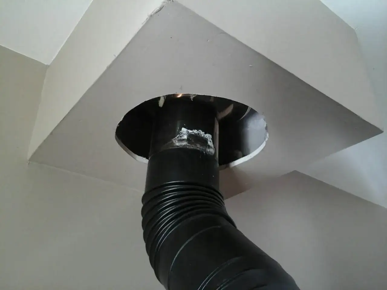 Conduit de cheminée noir traversant un faux plafond en placo. La distance entre le conduit et le placo est visible.