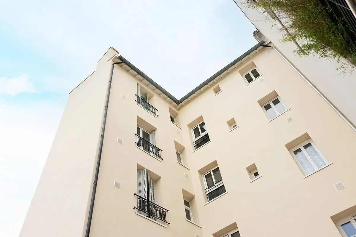 Fa&ccedil;ade d'immeuble r&eacute;nov&eacute;e, soulignant l'obligation d'isolation thermique en copropri&eacute;t&eacute;. Ciel bleu et verdure en arri&egrave;re-plan.