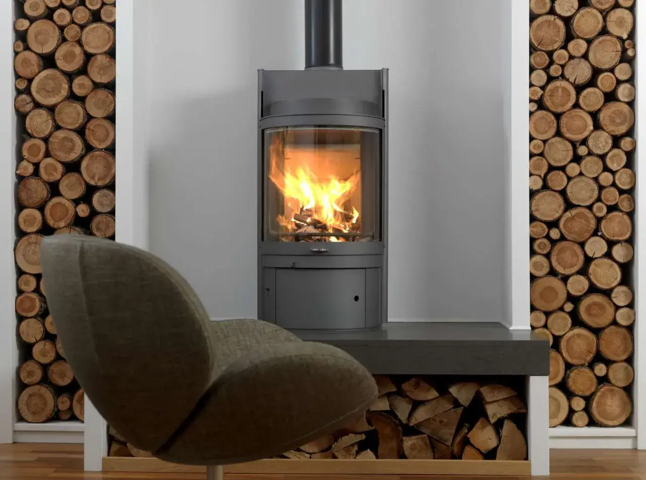 Un fauteuil confortable devant un poêle moderne, offrant un chauffage sans électricité, avec des bûches empilées décorativement.