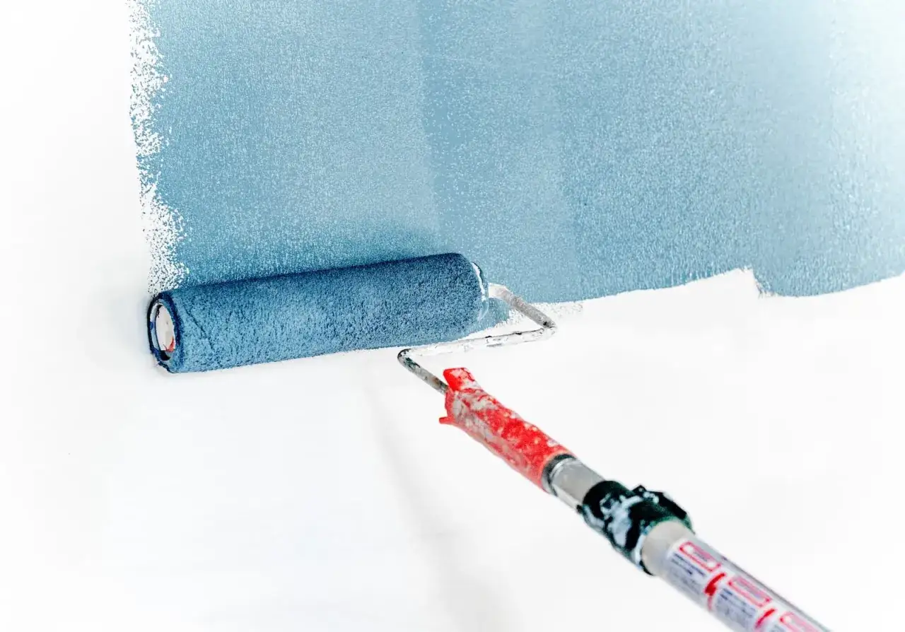 Un rouleau bleu est utilisé pour peindre un mur en bleu clair. La peinture est appliquée en larges bandes.