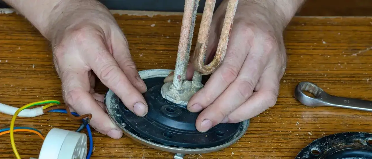 Réparation d'un chauffe-eau : les mains ajustent la résistance et le joint rouge, suspectant une fuite par le haut. Outil à proximité.