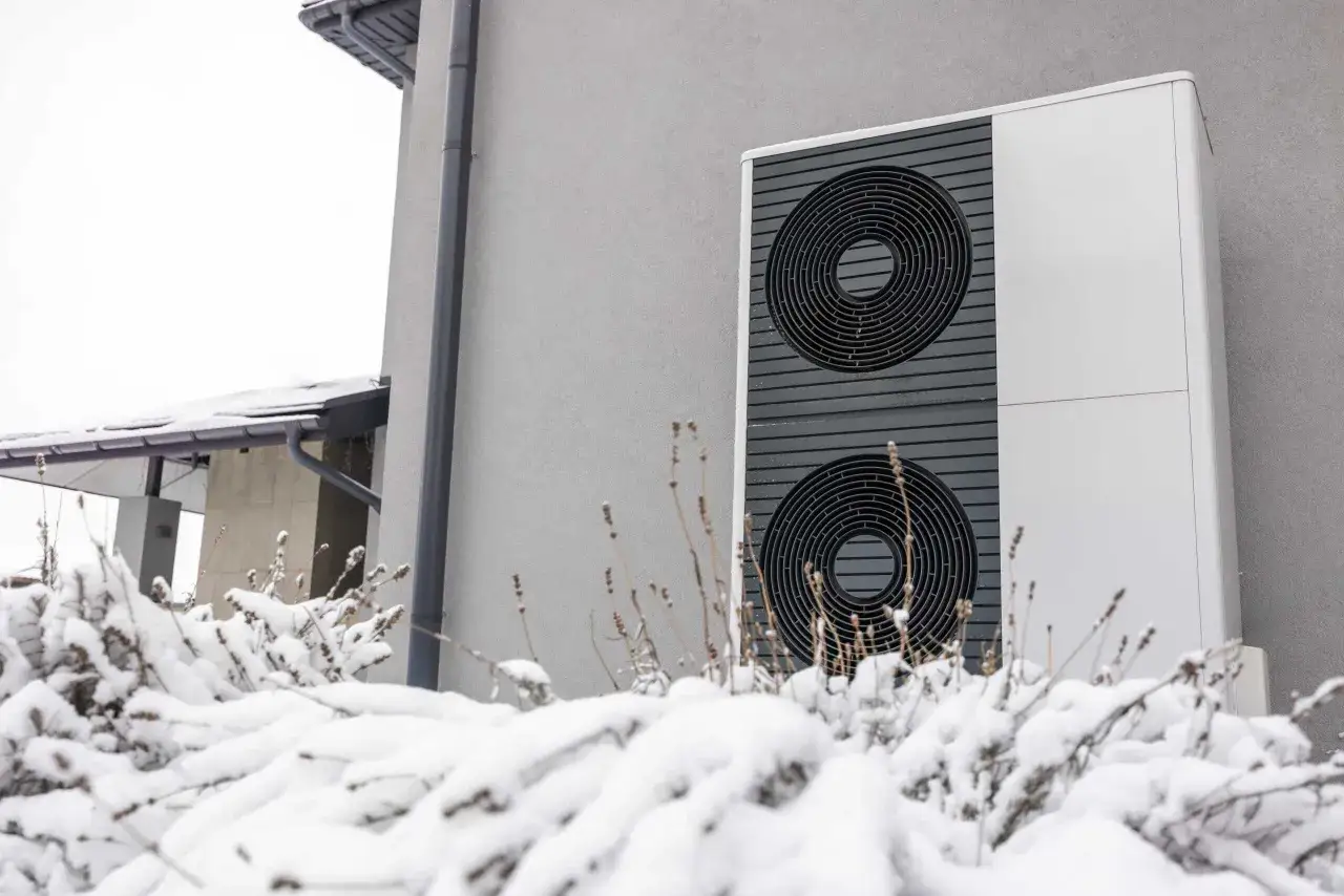 Unité extérieure de pompe à chaleur devant une maison, recouverte de neige. La pompe à chaleur ne chauffe pas quand il fait froid.