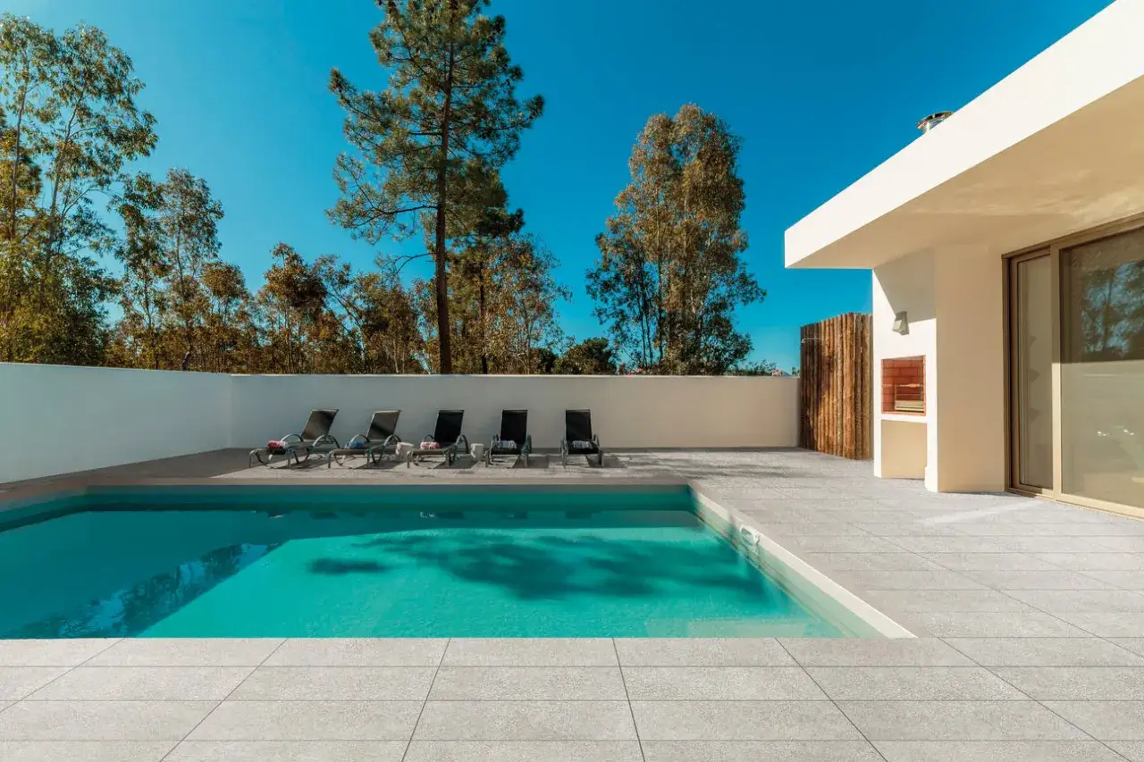 Une piscine moderne avec des chaises longues et un espace barbecue, le tout entouré d'un sol impeccable pour carreler une piscine.