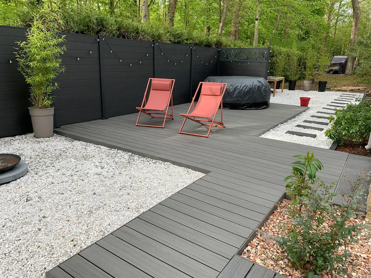 Une pose terrasse bois sur terre, avec deux chaises pliantes corail, un spa bâché et un chemin de dalles blanches.