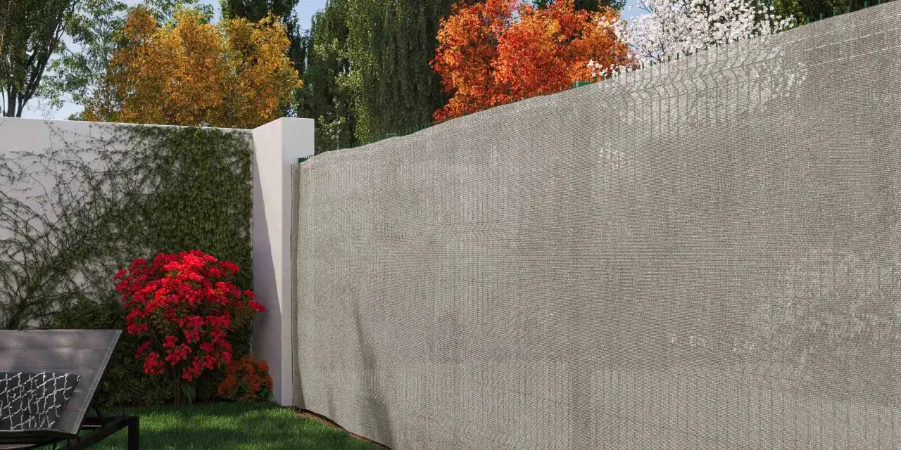 Un jardin paisible avec un mur blanc couvert de lierre, des fleurs rouges &eacute;clatantes et un pose brise vue gris pour plus d'intimit&eacute;.