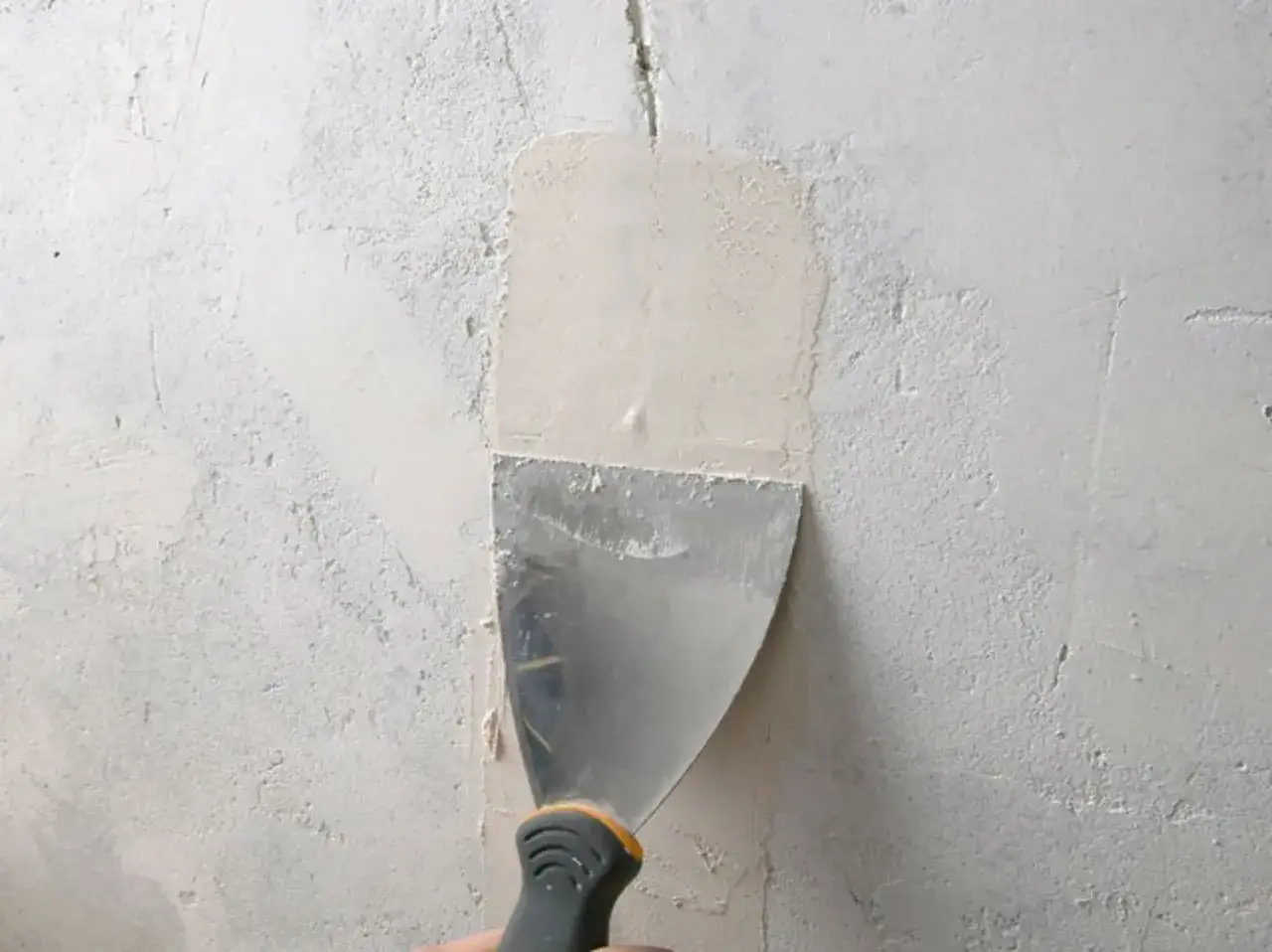 Application d'enduit avec une spatule pour comment reboucher une fissure dans un mur.