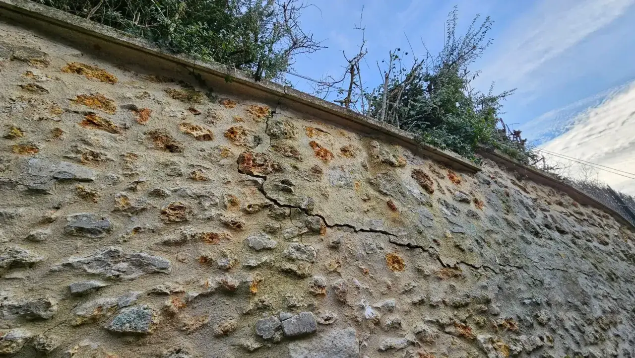 Un mur mitoyen en pierres présente une fissure importante. Des travaux de réparation sont nécessaires pour sécuriser la structure.