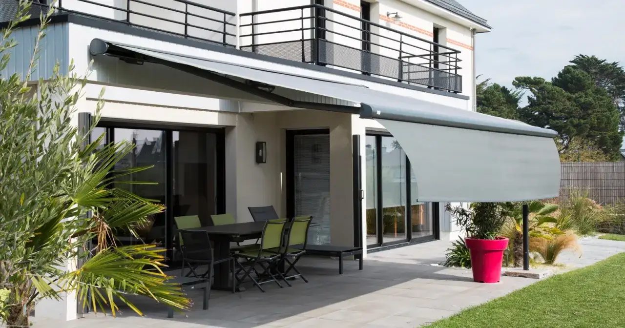 Un store banne gris protège une terrasse moderne avec mobilier de jardin. Parfait pour profiter de l'extérieur.