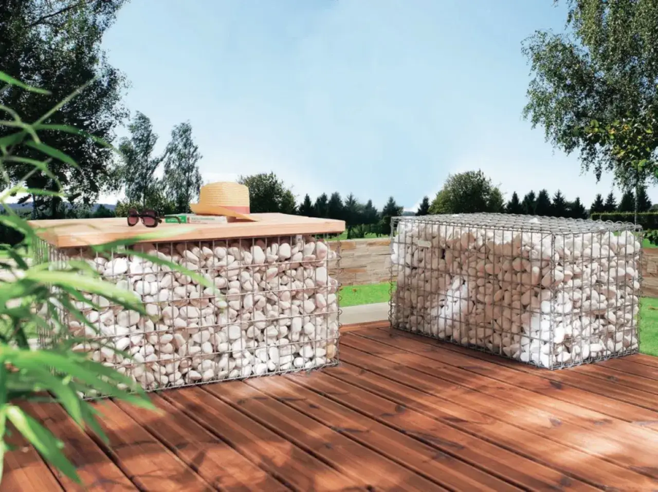 Un jardin en pente moderne avec des éléments en gabions remplis de pierres blanches. Un chapeau de paille et des lunettes de soleil reposent sur un plateau en bois.