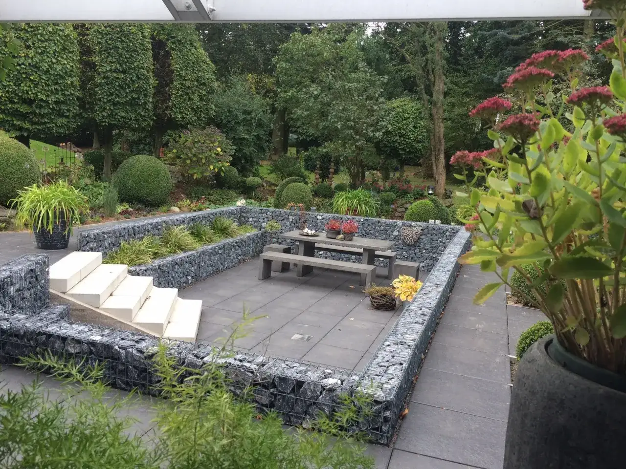 Un jardin en pente moderne avec des murs en gabions, une terrasse pavée, des escaliers en pierre et un coin repas.