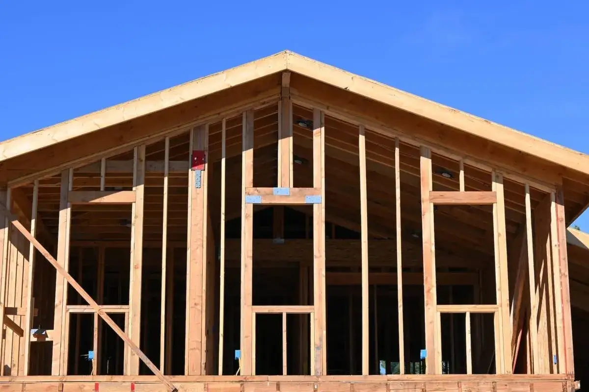 Structure en bois d'une maison en cours d'agrandissement. Le squelette de bois est visible sous un ciel bleu clair.