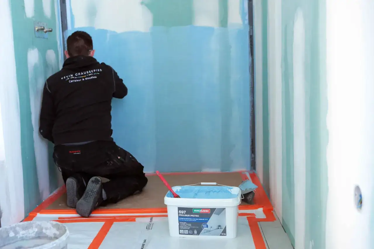 Un carreleur applique un produit d'étanchéité sur un mur, préparant une salle de bain pour une pose de carrelage.