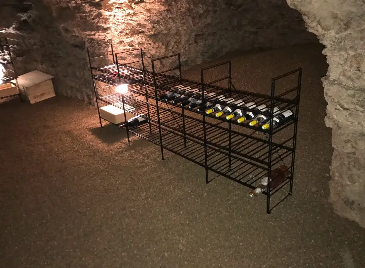 &Eacute;tag&egrave;res m&eacute;talliques remplies de bouteilles de vin dans une cave humide. Un ventilateur est visible, assurant la circulation de l'air.
