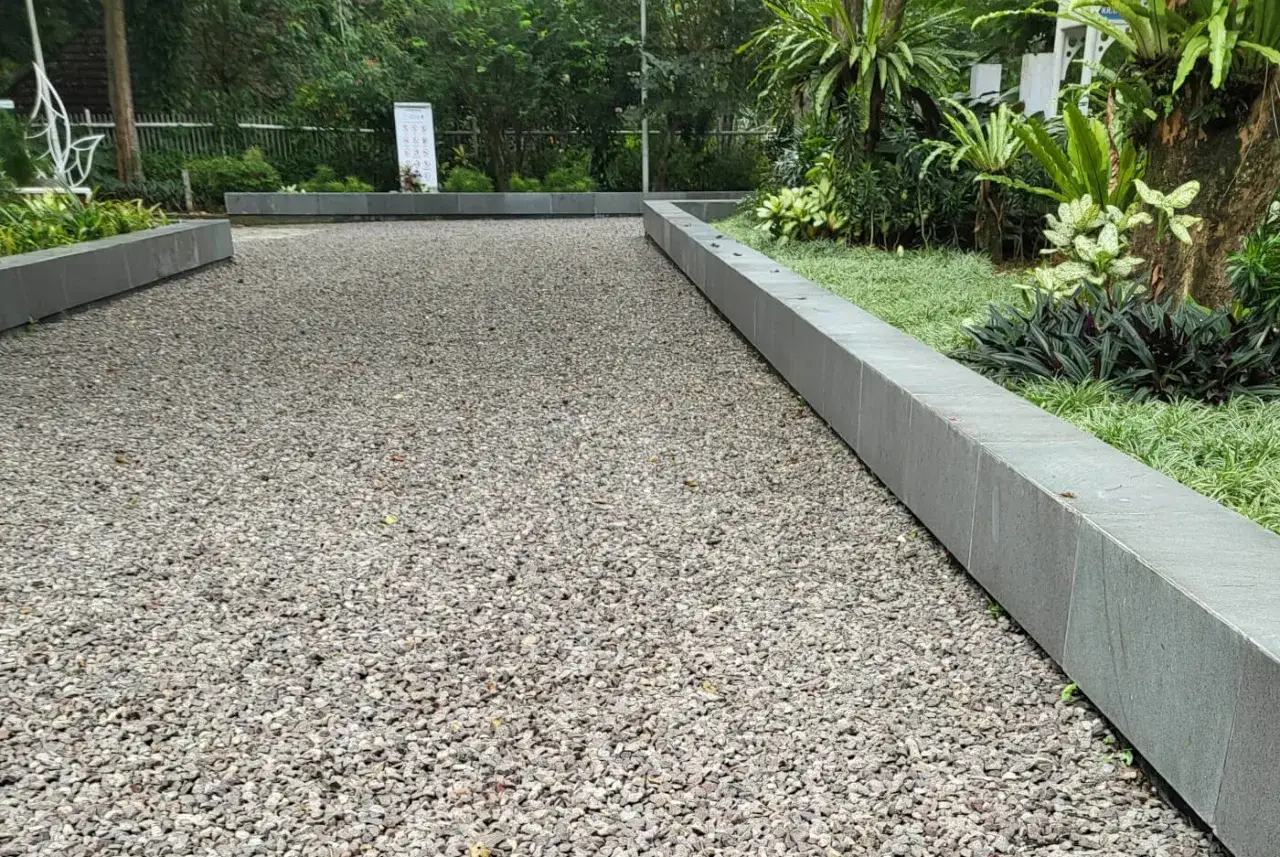 Un chemin de gravier m&egrave;ne &agrave; un jardin luxuriant. Le parking en gravier est bord&eacute; de dalles de pierre et de v&eacute;g&eacute;tation tropicale.