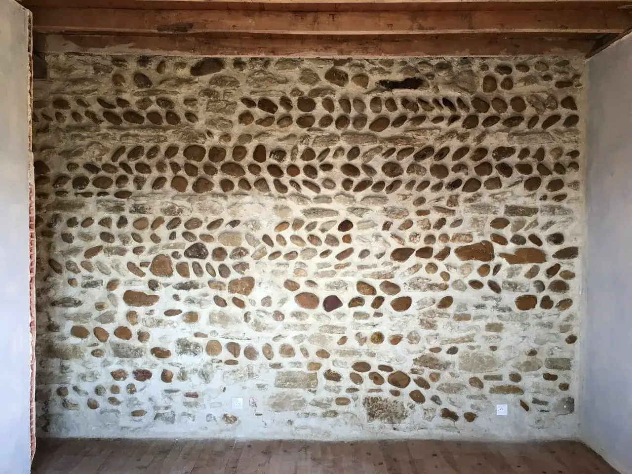 Mur en pierre de rivière avec un mortier clair. La couleur du joint du mur en pierre met en valeur les galets de différentes tailles et teintes.